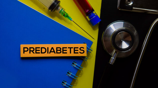 Note paper with word prediabetes printed on it sits on pad of paper with a needle, blood sample, and stethoscope sitting nearby