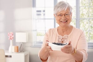 Smiling senior woman holds a bowl of brain supporting blueberries