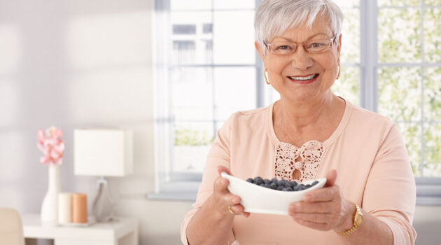 Smiling senior woman holds a bowl of brain supporting blueberries