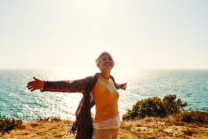 Senior woman with her arms outstretched at the beach in the sunlight