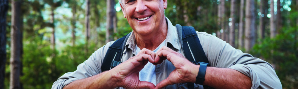 Shot of a mature man forming a heart shape with his hands while out hiking