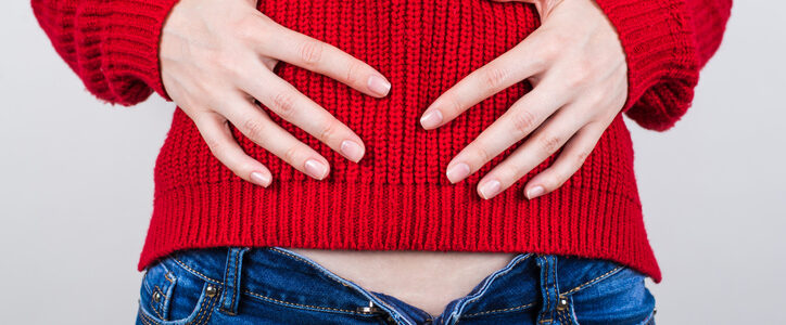 Women with open jeans and red sweater holds belly because of bloating