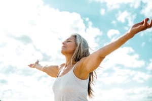 Joyful senior woman standing with open arms outdoors.