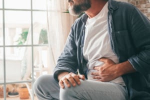 Man holding his stomach in discomfort while sitting