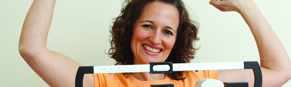 Happy mature woman rising her arms on a medical weight scale.