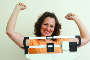 Happy mature woman rising her arms on a medical weight scale.