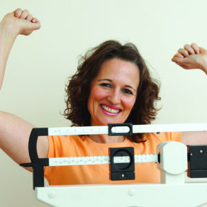 Happy mature woman rising her arms on a medical weight scale.