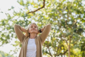 Happy mature woman who beat depression takes a deep breath as she walks in park under trees