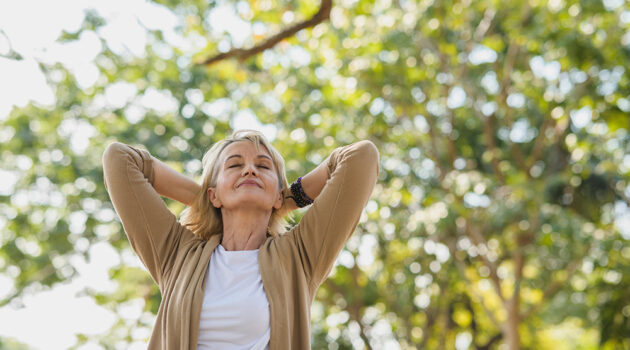 Happy mature woman who beat depression takes a deep breath as she walks in park under trees