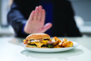 Close-up of a man's hand refusing to eat hamburger and French fries.