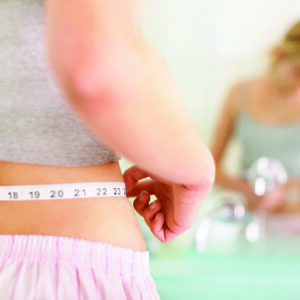 Closeup of a young woman measuring her waist in the bathroom