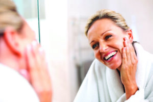 Happy mature woman looking at her skin in the mirror