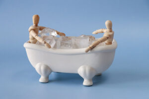 Two wooden figurines sit in plstic bath with ice cubes to illustrate cold therapy