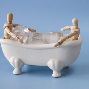 Two wooden figurines sit in plstic bath with ice cubes to illustrate cold therapy