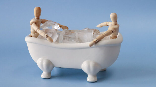 Two wooden figurines sit in plstic bath with ice cubes to illustrate cold therapy