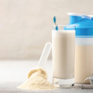 Whey protein powder and mixing bottle with a glass and a straw