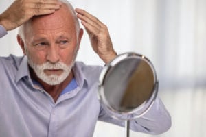 Senior man checking his hairline looking at mirror.